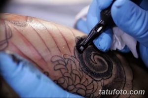 Фото процесса нанесения татуировки на руку. Виден тату-аппарат и рука мастера в перчатке, работающего над эскизом.